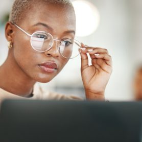 woman wearing glasses and reading serious article on laptop in professional setting.