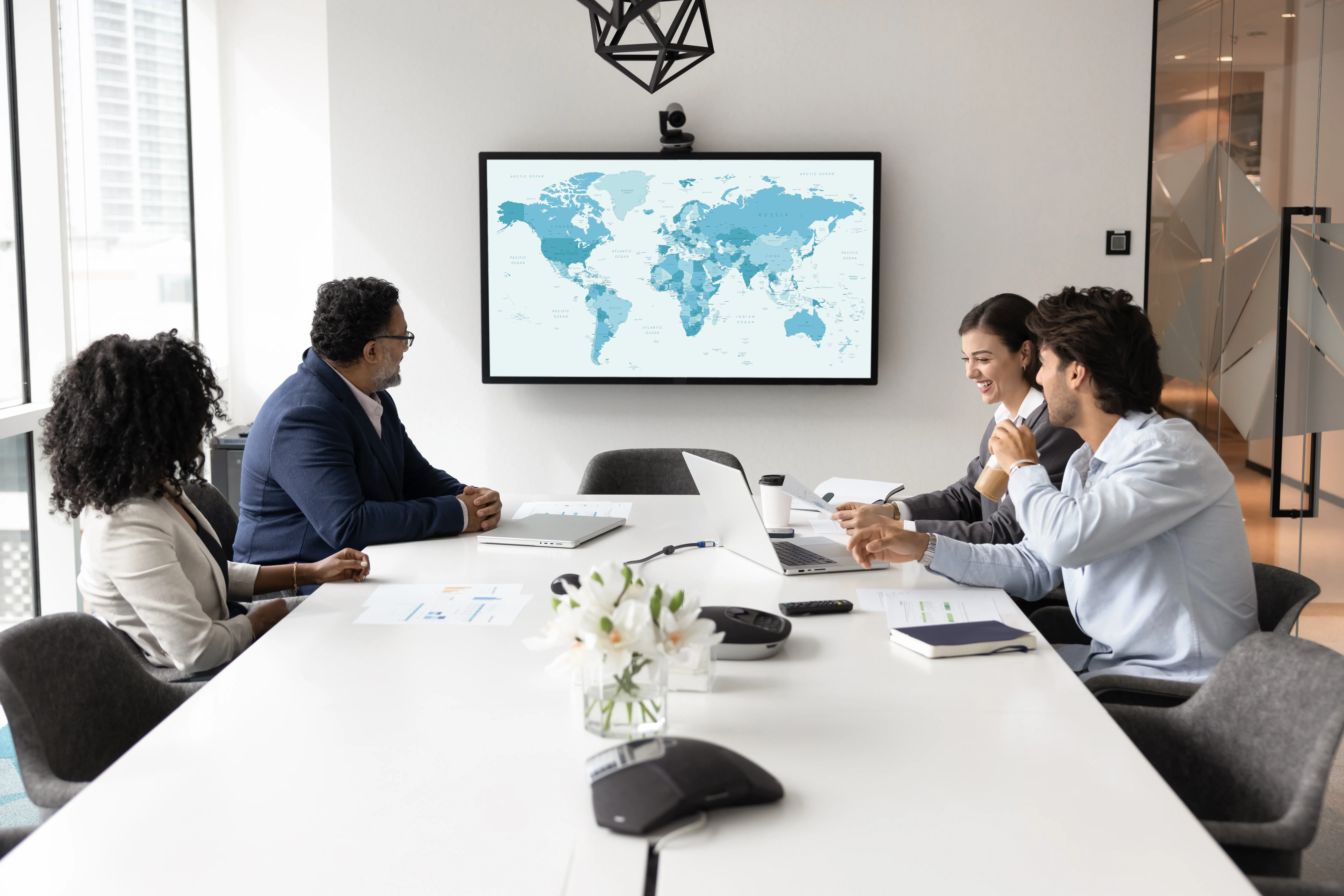 A group of four Alimentiv global strategy experts sitting in a bright conference room, reviewing a world map displayed on a large screen during a meeting.
