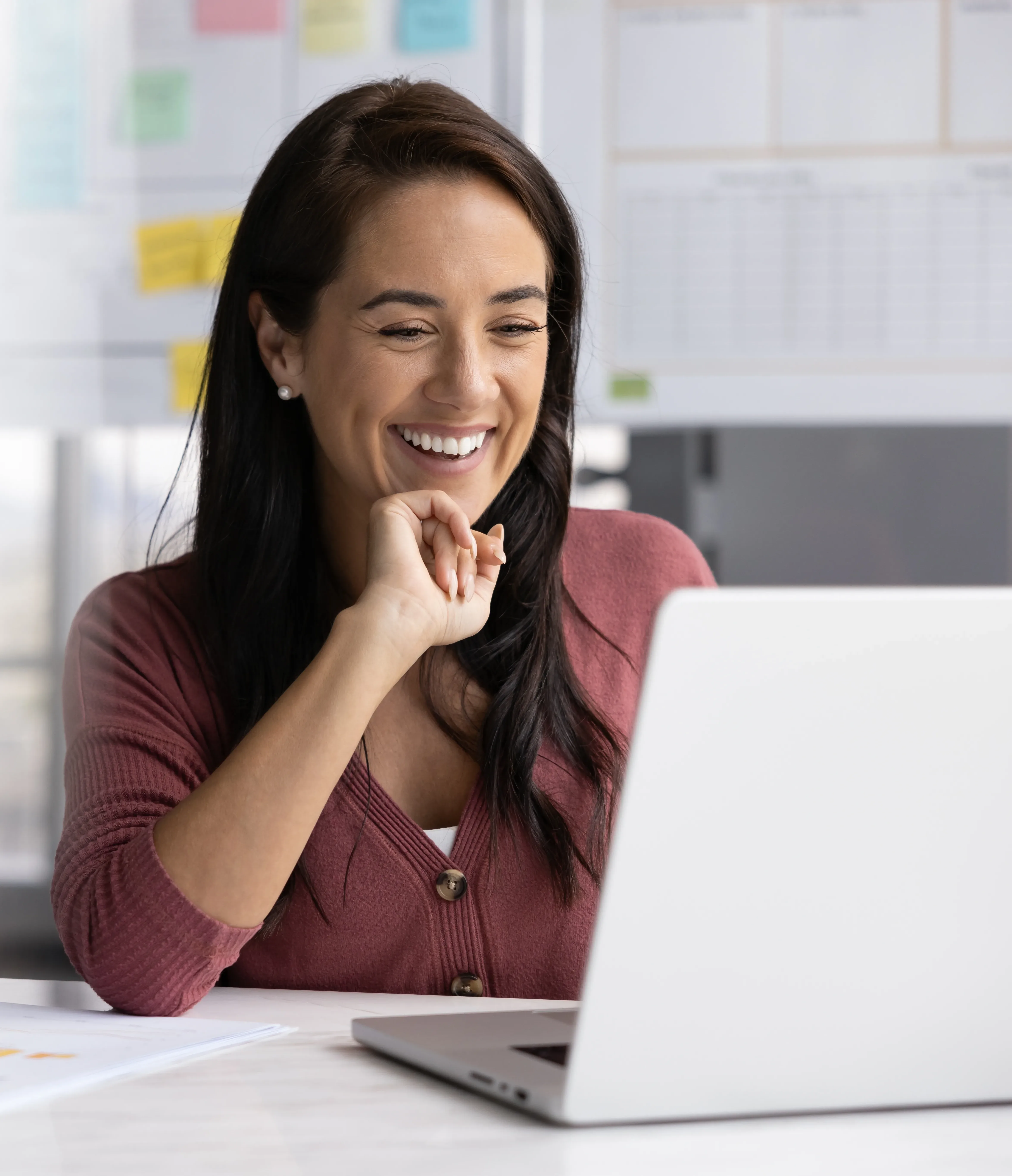 A smiling Alimentiv project manager in a mauve cardigan reviewing clinical trial deliverables on a laptop in a bright, modern office.