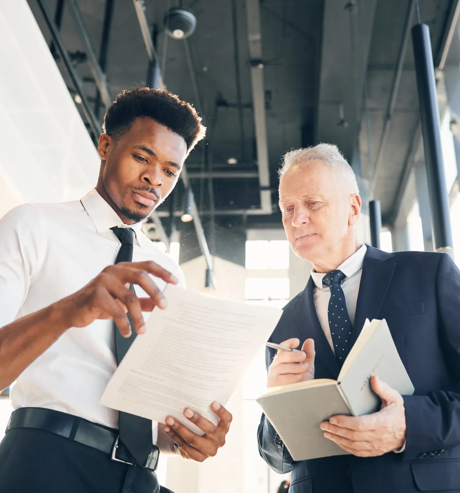 Two business professionals stand in a bright modern office reviewing printed documents and notes together, engaged in focused discussion and decision making, representing leadership and collaboration at Alimentiv