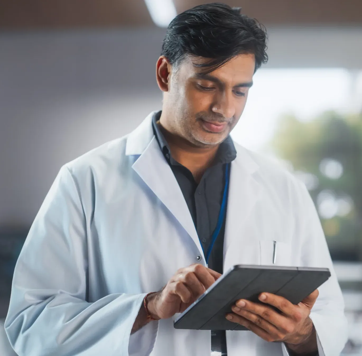 A healthcare professional in a white lab coat uses a tablet in a modern laboratory while colleagues work in the background, representing digital data management and clinical research at Alimentiv
